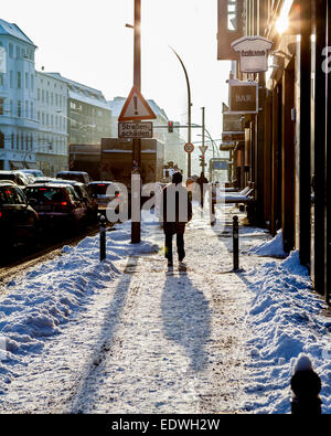 Mann zu Fuß entlang der schneebedeckten Fahrbahn in hellem Sonnenlicht im Winter, Mitte, Berlin, Deutschland Stockfoto