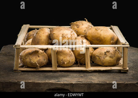 Junge Reife Kartoffeln in einer Holzkiste auf dem dunklen Hintergrund Stockfoto