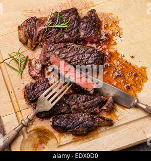 Gegrilltes Entrecote mit mit Messer und Gabel auf Fleisch Schneidbrett auf hölzernen Hintergrund Stockfoto