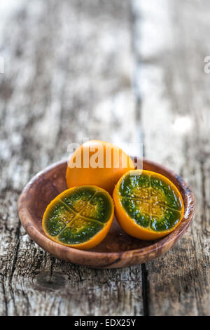 Schneiden Sie lebendige Grün und orange konkretisiert Lulo in eine hölzerne Schüssel auf rustikalen Holztisch Stockfoto