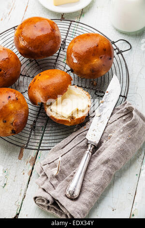 Hausgemachte Brötchen mit Rosinen auf Kuchengitter abkühlen auf blauem Hintergrund aus Holz Stockfoto