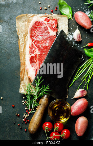 Vintage Cleaver und rohes Rindfleischsteak auf dunklem Hintergrund Stockfoto