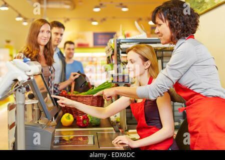 Ältere Verkäuferin helfen junge Frau an der Supermarktkasse Stockfoto