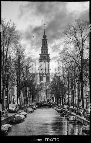 Winter in Amsterdam, Stadtbild von Hausbooten entlang des Kanals an einem nebeligen Tag, eine schöne Kirchturm im Hintergrund Stockfoto