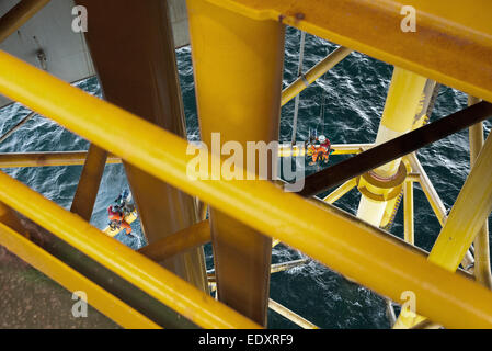 Gelbes Stahlbauwerk einer Offshore-Öl- und Gasplattform über der Nordsee, im Hintergrund sichtbare Seilzugangstechniker. Stockfoto