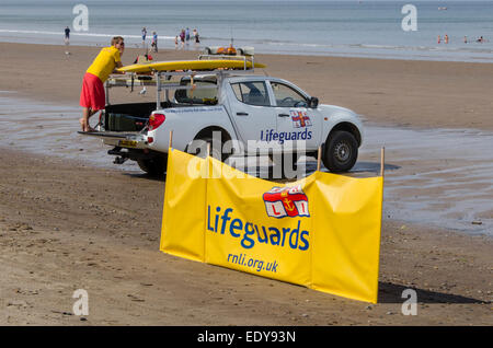 Junger Mann auf Pflicht als rnli Lifeguard ist gerade Menschen in Meer und steht auf der Rückseite des geparkten Pick-up Truck - Whitby Beach, North Yorkshire, England, UK. Stockfoto