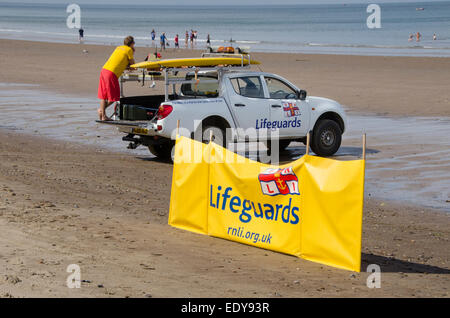 Junger Mann auf Pflicht als rnli Lifeguard ist gerade Menschen in Meer und steht auf der Rückseite des geparkten Pick-up Truck - Whitby Beach, North Yorkshire, England, UK. Stockfoto