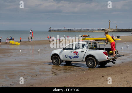 Junger Mann auf Pflicht als rnli Lifeguard ist gerade Menschen in Meer und steht auf der Rückseite des geparkten Pick-up Truck - Whitby Beach, North Yorkshire, England, UK. Stockfoto