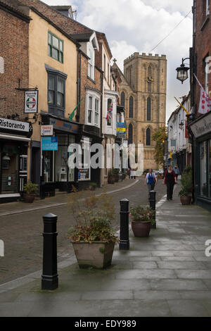 Blick nach unten schmal, historischen Kirkgate, gesäumt von kleinen Geschäften, hin zu einem Turm an der Westseite von Ripon Cathedral - North Yorkshire, England, UK. Stockfoto