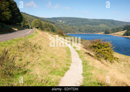 Straße und Gehweg neben Ladybower Vorratsbehälter führt in Richtung Fairholmes an einem hellen, sonnigen Tag. Stockfoto