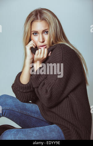 Hübsche junge Frau am Boden mit Pullover. Attraktive Frau schaut in die Kamera gegen die weiße Wand. Stockfoto