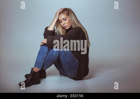 Nachdenkliche Frau in Pullover am Boden. Studioaufnahme jungen Frau ernst mit Exemplar Stockfoto