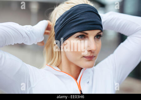 Nahaufnahme der jungen Sportlerin, die Haare vor einem Lauf zu binden. Sportliche Fitness Frau auf outdoor-Training suchen motivierten. Stockfoto