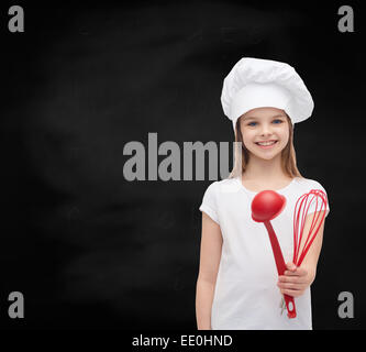 lächelndes Mädchen in Koch Hut mit Kelle und Schneebesen Stockfoto