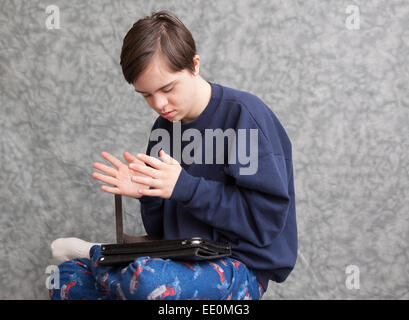 Teenager mit Autismus und Down-Syndrom, klatschte in die Hände wie er mit einem Tablet spielt Stockfoto