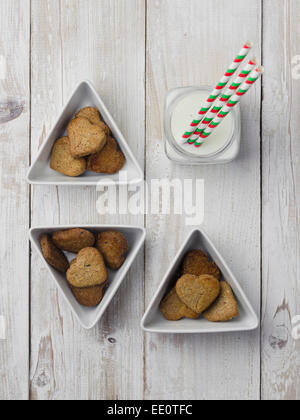 Hausgemachte herzförmige Kekse und Milch über weißen Holztisch Stockfoto