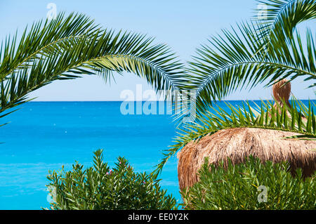 Thatched Dach Bungalows auf einem Hintergrund von blauem Meer und Palmen Stockfoto