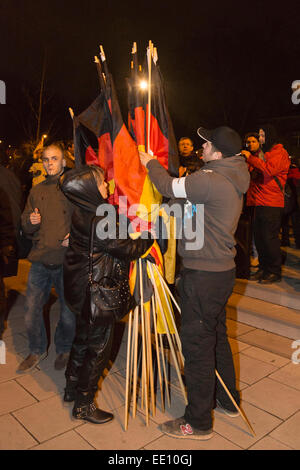 01.05.2015. Köln, Deutschland. Ein Demonstrant rechten Kupplungen deutsche Nationalflaggen vor Aushändigung sie Unterstützer. Etwa zwei hundert rechtsextreme Demonstranten folgte einem Ruf zu demonstrieren gegen die Islamisierung Europas in Köln. KÖGIDA Demonstranten wurden von Tausenden von linksgerichteten Demonstranten weit unterlegen. Dies folgt der PEGIDA-Demonstrationen in Dresden, die eine große Zahl von Anhängern anzuziehen, zu halten. PEGIDA steht für "Patriotischen Europäische gegen die Islamisierung Europas". Wie ein Protest, Kölner Dom - in der Regel beleuchtet in der Nacht - im Dunkel blieb protestieren ag Stockfoto