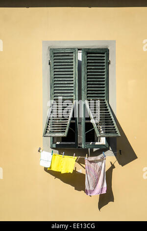 Fenster in eine gelbe Wand mit verwitterten grünen Fensterläden & eine Linie gelb rosa weiße Handtücher unter trocknen in der Sonne Lucca Italien Stockfoto