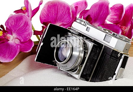 Antike 35mm Film-Kamera im weißen Sand mit rosa Orchideen Stockfoto