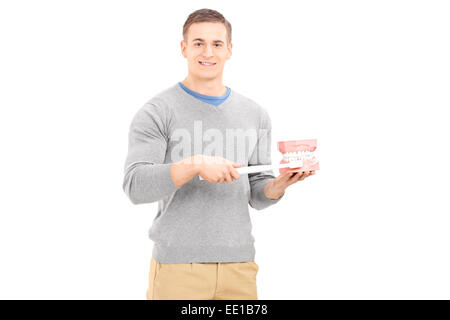 Junger Mann hält einen riesigen Prothese und Zahnbürste isoliert auf weißem Hintergrund Stockfoto