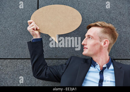 Junger Geschäftsmann hält leere Sprechblase vor einer Wand Stockfoto