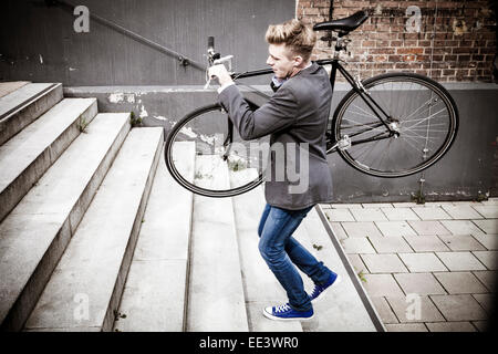 Junger Geschäftsmann mit dem Fahrrad über Treppen, München, Bayern, Deutschland Stockfoto