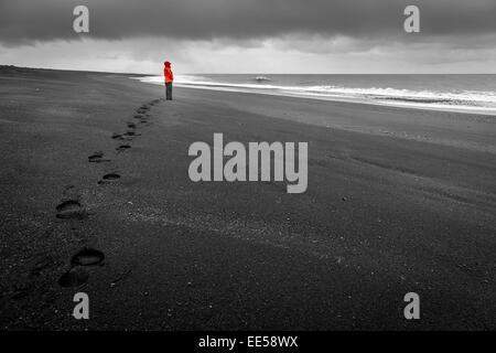 Eine Frau beobachtet die Wellen auf einem schwarzen Sandstrand im Süden von Island Stockfoto