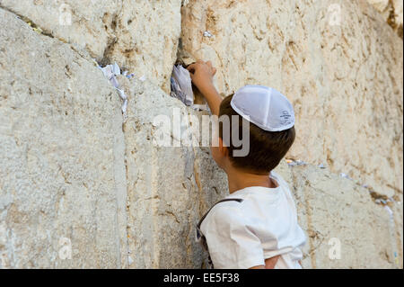 JERUSALEM, ISRAEL - 6. Oktober 2014: Ein kleiner jüdischer Junge ist eine Papier mit einem Wunsch in einen Spalt zwischen den Steinen der westlichen setzen Stockfoto