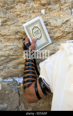 JERUSALEM, ISRAEL - 6. Oktober 2014: Ein jüdischer Mann mit der Thora in seiner Hand und Tefillin um seinen Arm gegen die Wes betet Stockfoto