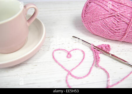 Rosa häkeln Hintergrund mit Herz und Kaffee Tasse Garn und Häkelnadel auf hölzernen Hintergrund Stockfoto