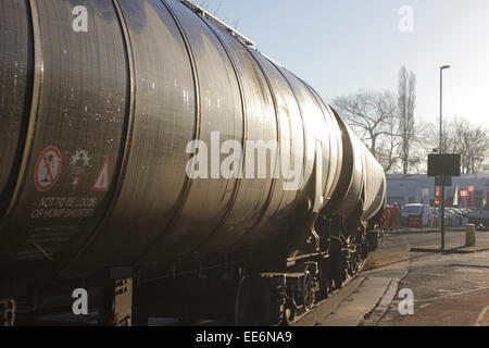 Am Vormittag hell und frostigen Dezember funkelt das Sonnenlicht aus einem Zug leeren Bitumen Tank Eisenbahnwaggons Strand Straße Preston überqueren. Stockfoto