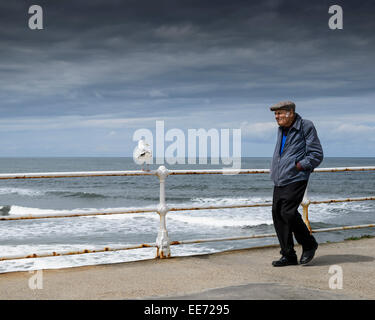 Ein älterer Mann Whitby Pier mit der Nordsee im Hintergrund und ein bewölkter Himmel entlang. Stockfoto