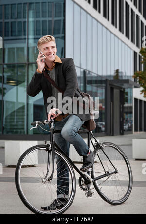 Junger Geschäftsmann mit dem Fahrrad mit Handy, München, Bayern, Deutschland Stockfoto