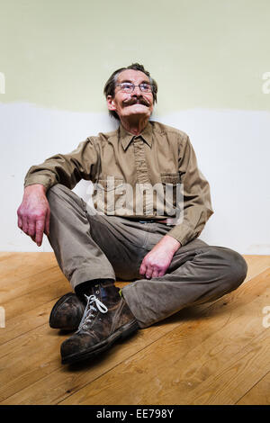 Der Mensch in seiner 60er Jahre mit Schnurrbart tragen khakifarbene Hemd und Hose auf dem Boden sitzen. Stockfoto