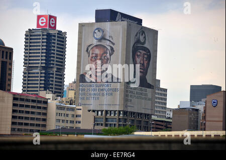 Die Gesichter der Bergleute auf einem Wolkenkratzer in der Innenstadt von Johannesburg betrachtet aus der Ferne. Stockfoto