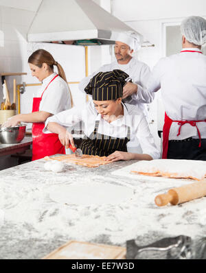 Koch schneiden Ravioli Pasta mit Kollegen im Hintergrund Stockfoto