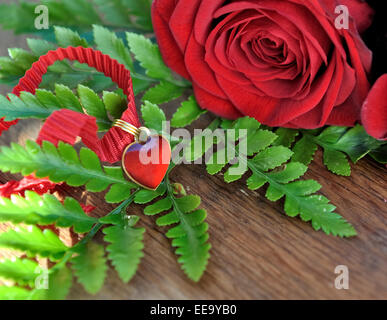 Herz-Anhänger auf Laub mit roten Rosen auf hölzernen Hintergrund Stockfoto