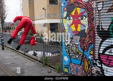 Mann verkleidet als Weihnachtsmann über einen Zaun in der Nähe von Brick Lane, London, UK springt. Wie Weihnachten zu Ende geht wird er gesehen, Weg zu laufen, als ob irgendeine Art von Straftat schuldig. Stockfoto