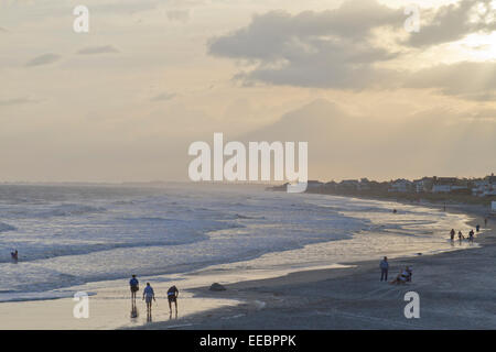 Entspannte Menschen wandern am Strand und im Meer in der Dämmerung spielen Stockfoto