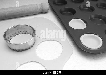 Auskleidung der Bun-Dose mit Kreisen von ausgerollt Gebäck zu Mince Pies, mit einem Nudelholz auf der Arbeitsplatte - monochrome Verarbeitung Stockfoto