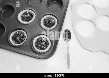 Mince Pies machen in der Küche - gefüllte Gebäck Fällen, Hackfleisch, Teig Fetzen und TL - monochrome Verarbeitung Stockfoto