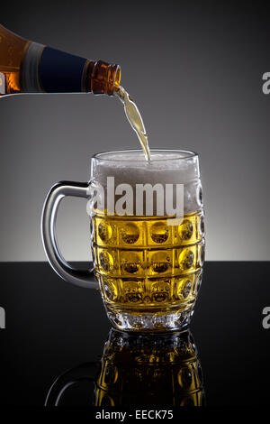 Bier aus der Flasche auf dem dunklen Hintergrund gegossen Stockfoto