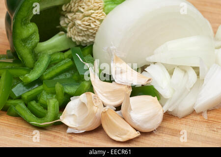 Knoblauchzehen mit gewürfelten Zwiebeln und grünem Paprika auf ein Holz Schneidebrett. Stockfoto