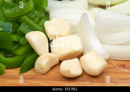 Knoblauchzehen mit gewürfelten Zwiebeln und grünem Paprika auf ein Holz Schneidebrett. Stockfoto