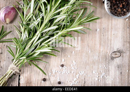 Frischen Haufen von Rosmarin, Knoblauch, Pfeffer und Salz auf Holztisch. Aromatischen immergrünes Kraut, viele kulinarische - gebratenes Fleisch. Copysp Stockfoto