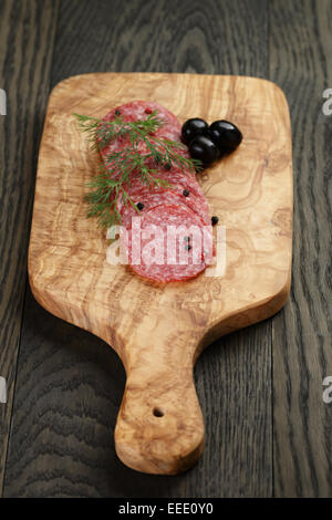 geschnittene Salami mit Pfeffer auf Oliven Brett auf Tisch Stockfoto