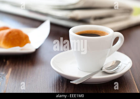 Tasse Kaffee auf Holztisch mit gestapelten Zeitungen im Hintergrund. Stockfoto