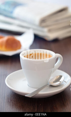 Tasse Kaffee auf Holztisch mit gestapelten Zeitungen im Hintergrund. Stockfoto