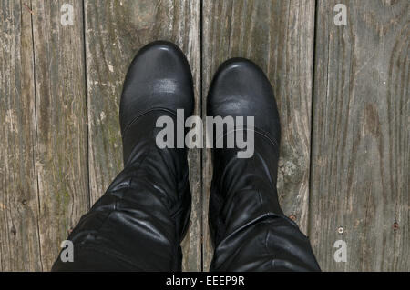 Woman's Füßen trug hohe schwarze Stiefel auf ein unbehandeltes Holz. Stockfoto